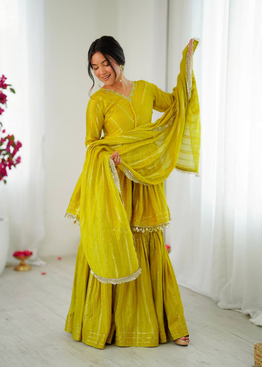 Side pose of mustard yellow sharara suit with golden stripes and dupatta, stylish Indian ethnic wear for women
