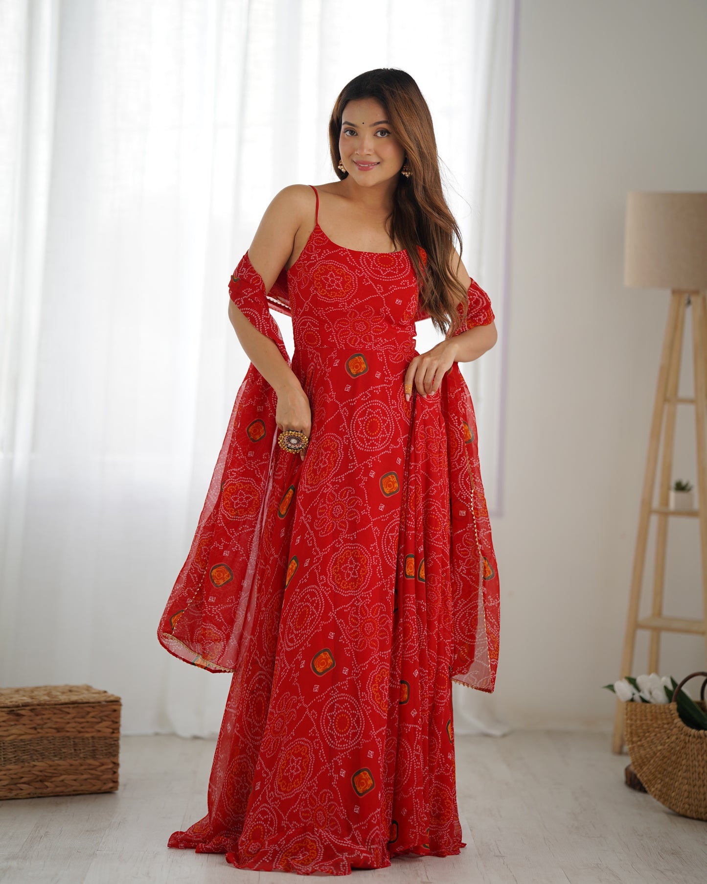 Woman wearing a red patterned dress in a room with white curtains and a lamp.