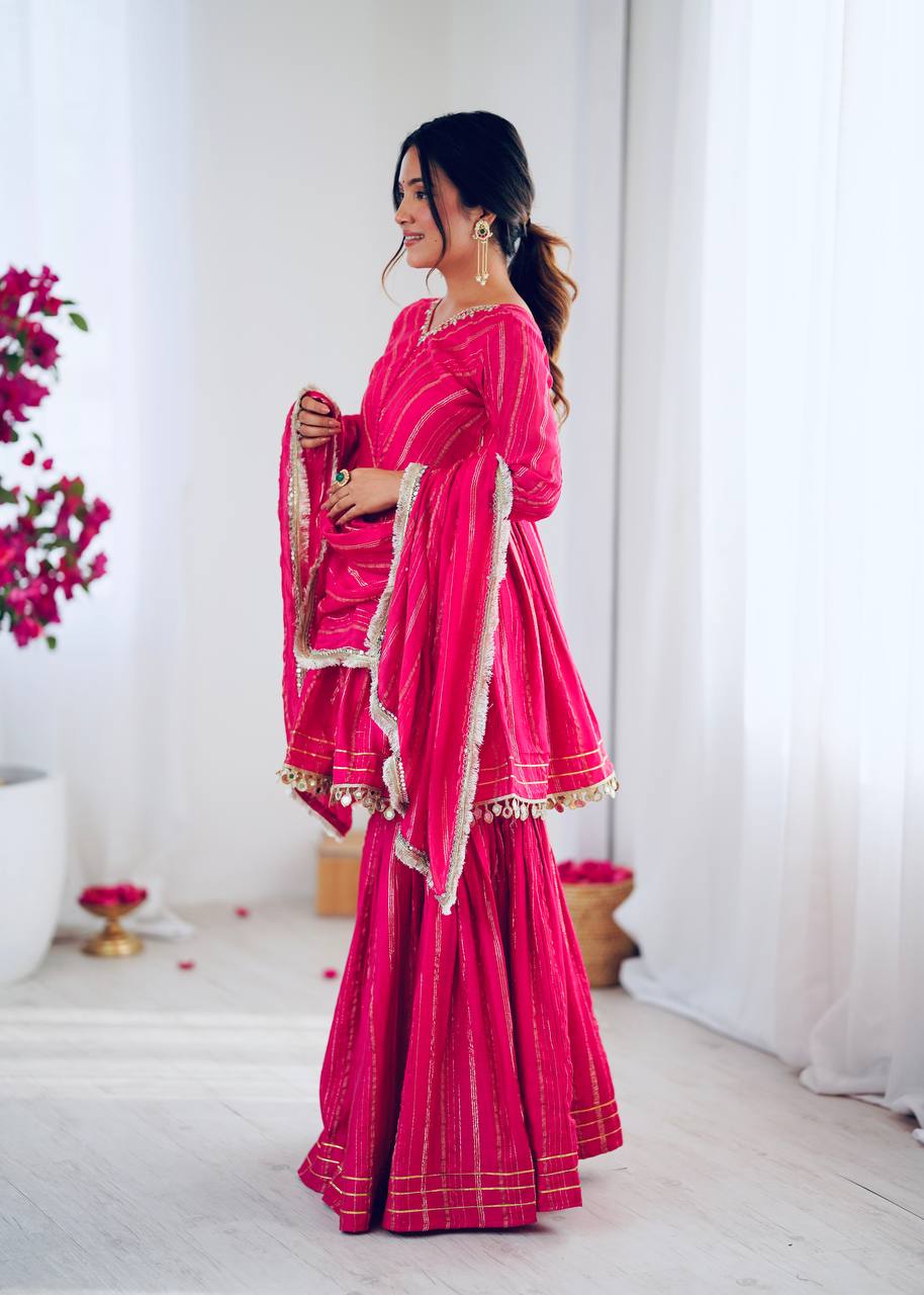 Side pose of rani pink sharara suit with golden stripes and dupatta, stylish Indian ethnic wear for women