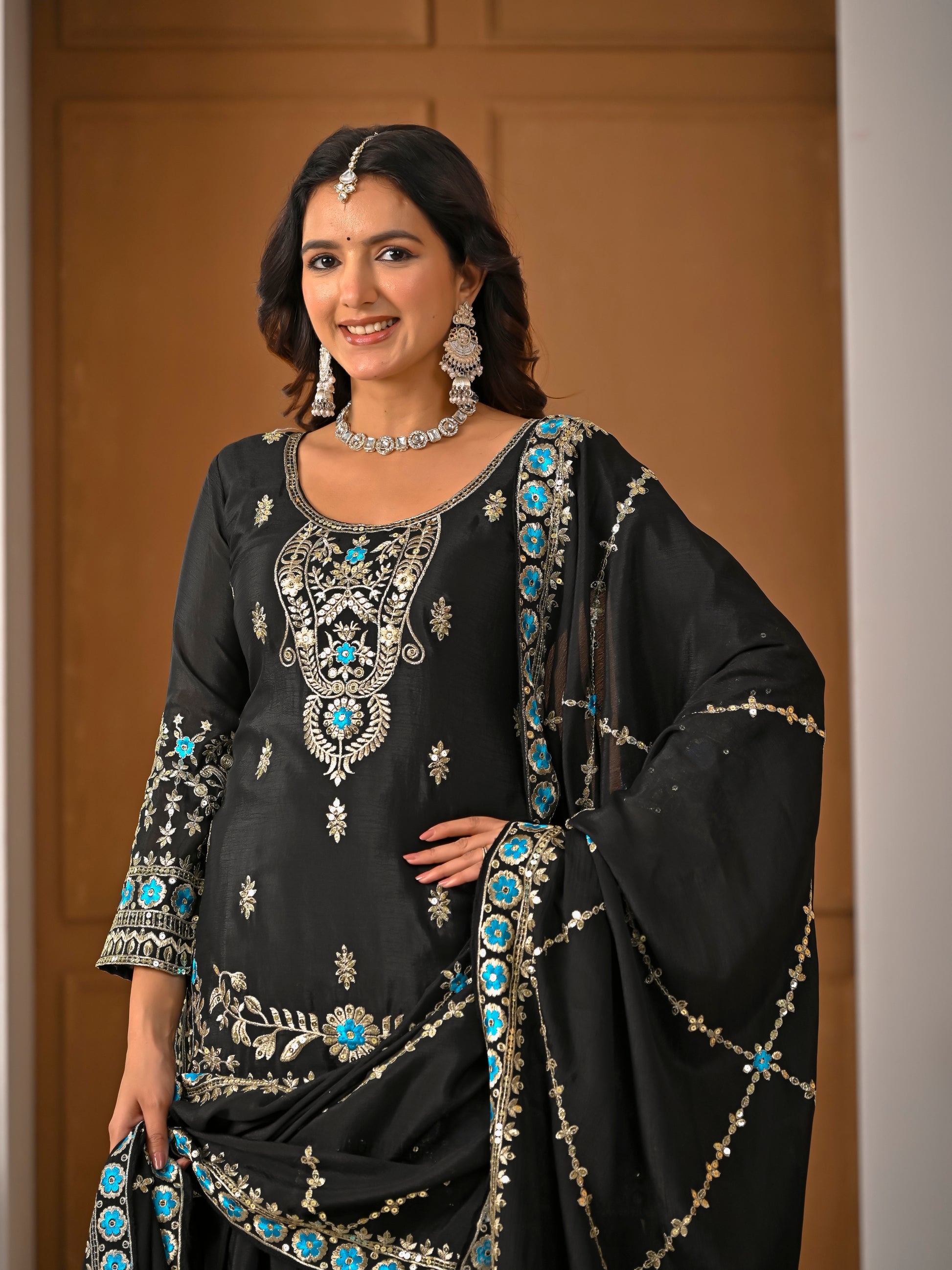 Woman wearing a black embroidered traditional outfit with turquoise stones against a neutral background