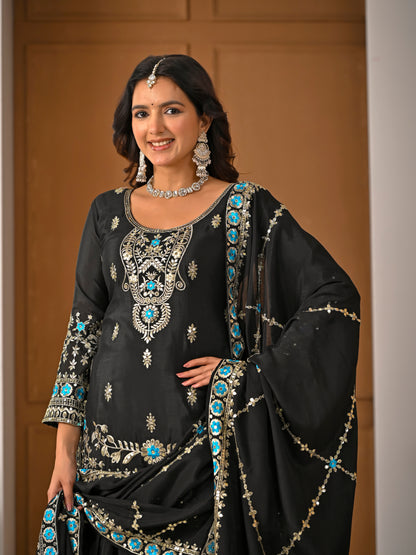 Woman wearing a black embroidered traditional outfit with turquoise stones against a neutral background